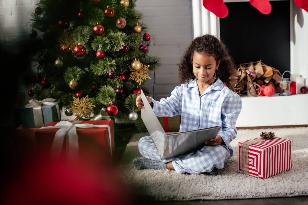 messa a fuoco selettiva di adorabile bambino afroamericano in pigiama libro di lettura vicino all'albero di Natale a casa
 - Foto, immagini