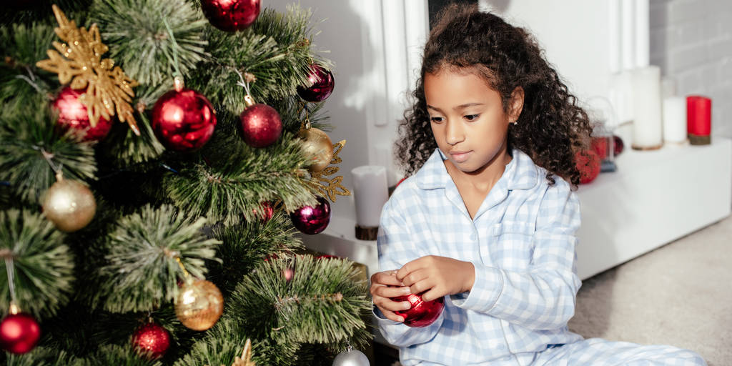 adorable enfant afro-américain en pyjama décorant l'arbre de Noël avec des boules rouges à la maison
 - Photo, image