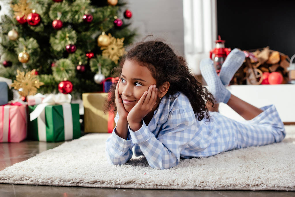 adorable african american child in pajamas lying on floor and looking away at home, christmas concept - Photo, Image