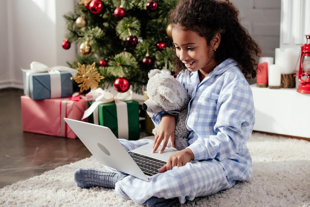 szczęśliwy adorable Afryki amerykański dziecko w piżamie z misiem w domu za pomocą laptopa christmas koncepcji - Zdjęcie, obraz