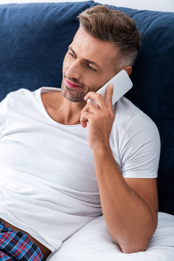 felice uomo adulto parlando su smartphone mentre sdraiato a letto a casa
 - Foto, immagini