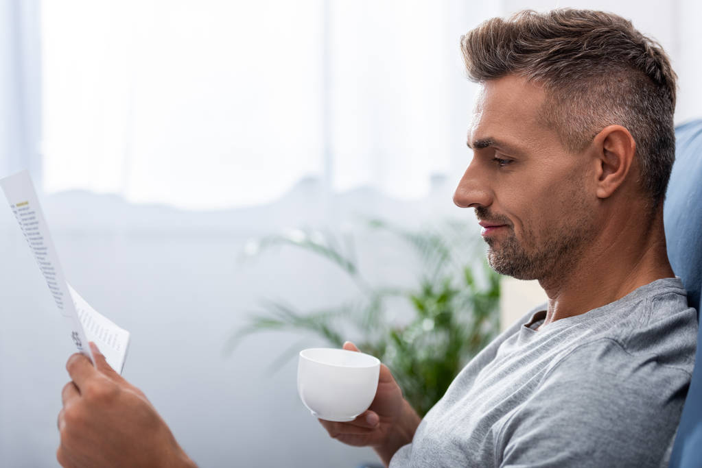 boční pohled podnikatel s šálkem kávy, čtení novin v posteli doma - Fotografie, Obrázek