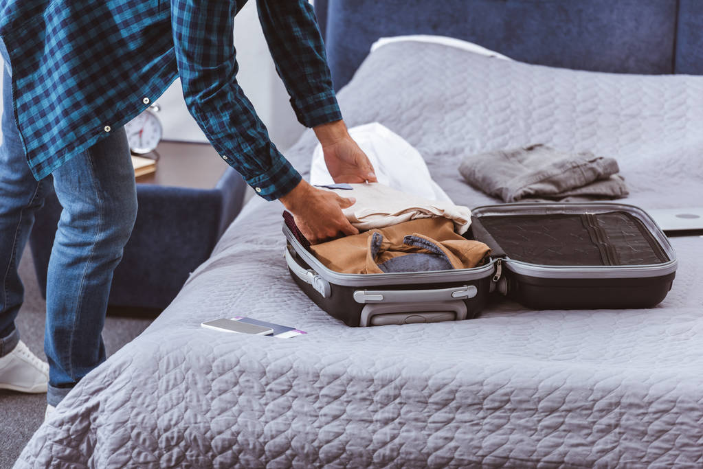 περικομμένη εικόνα αρσενικό ταξιδιώτη συσκευασίας αποσκευών στο υπνοδωμάτιο στο σπίτι  - Φωτογραφία, εικόνα