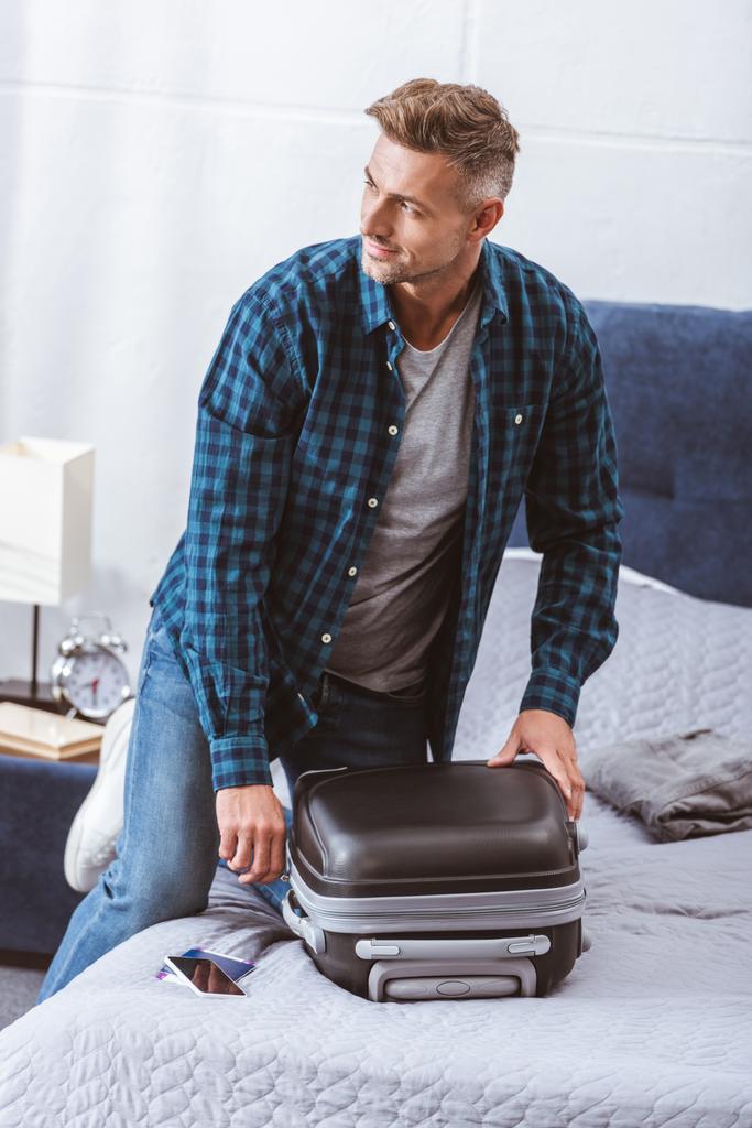 man packing travel bag and looking away in bedroom at home - Photo, Image