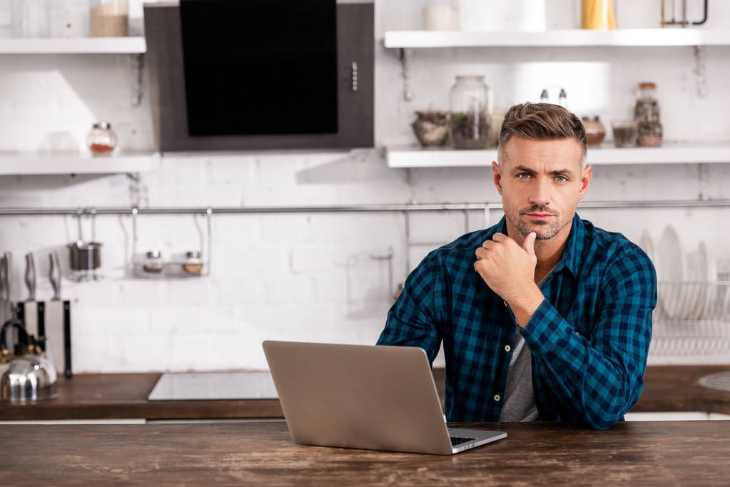 уверенный мужчина фрилансер, сидящий с ноутбуком за столом на кухне дома
  - Фото, изображение