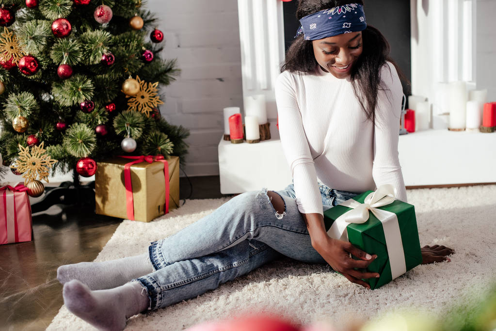 Gelukkig aantrekkelijke african american vrouw kijken thuis de gift van Kerstmis - Foto, afbeelding