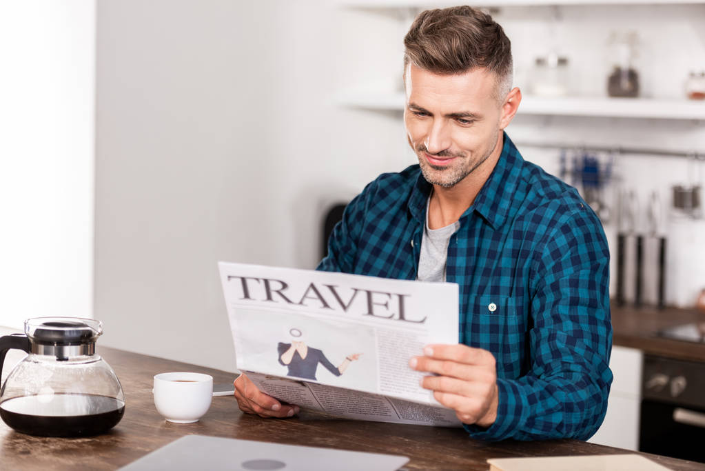 guapo sonriente hombre con camisa a cuadros leyendo el periódico de viaje por la mañana
 - Foto, imagen