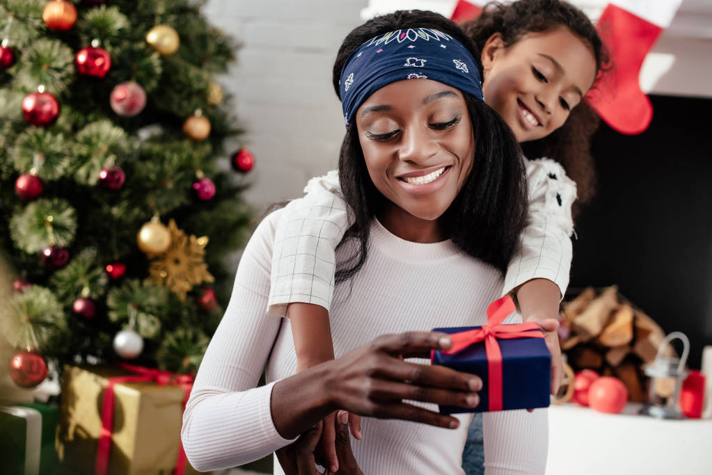 Afro-Amerikaanse dochter knuffelen en gifting kerstcadeau aan moeder thuis - Foto, afbeelding