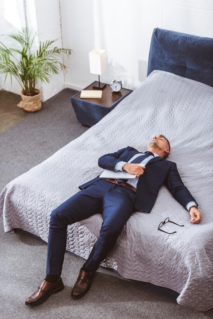 visão de alto ângulo de empresário sobrecarregado segurando laptop e deitado na cama
 - Foto, Imagem