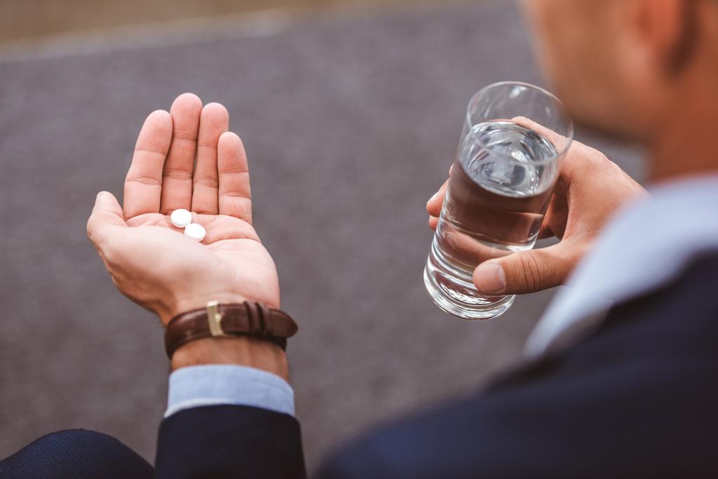 cropped shot of businessman in suit holding glass of water and pills   - Photo, Image