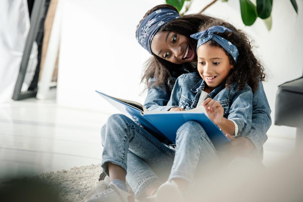 african american mother and smiling daughter looking at family photo album at home - Photo, Image