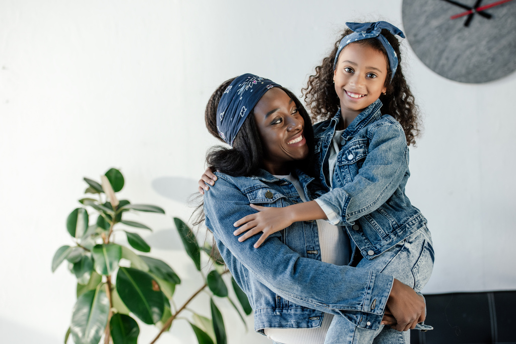 šťastný afroamerické ženy držící malou dceru v podobné oblečení na rukou doma - Fotografie, Obrázek