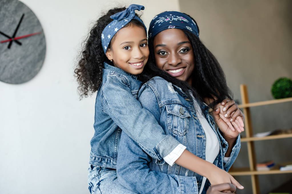 aranyos afro-amerikai gyerek átölelve mosolygó anya hasonló ruházati, otthon - Fotó, kép