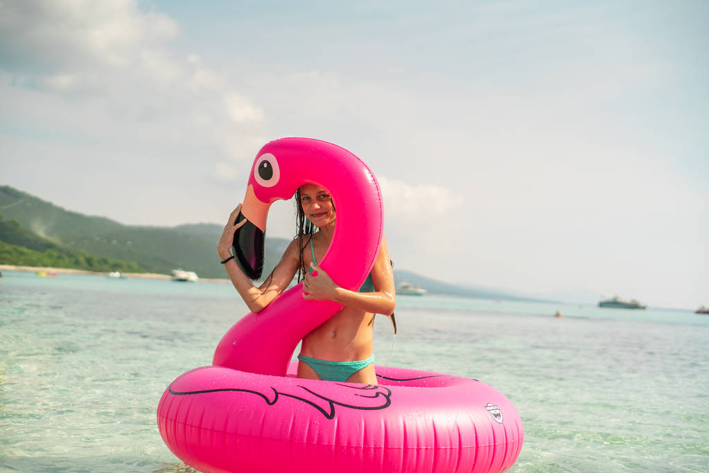 Portrait of young teenage girl with pink inflatable flamingo in the sea  - Photo, Image
