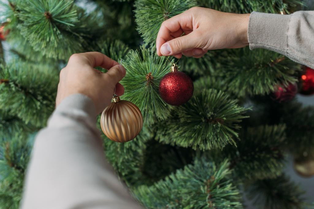 περικομμένη εικόνα του ανθρώπου που διακοσμεί χριστουγεννιάτικο δέντρο με στολίδια στο σπίτι - Φωτογραφία, εικόνα