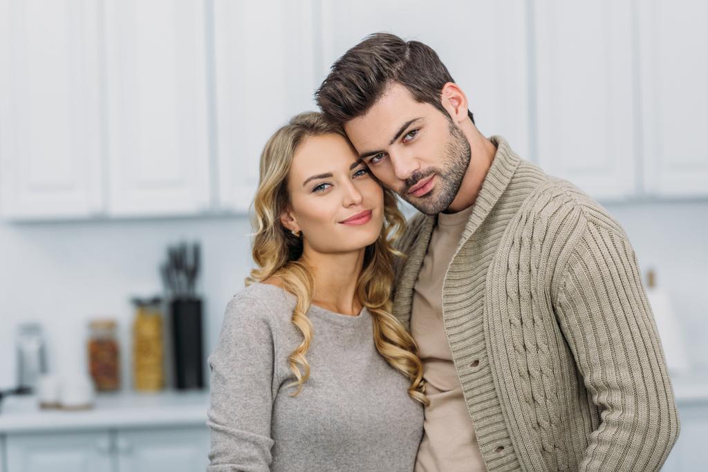 portrait of young couple hugging and looking at camera in kitchen - Photo, Image