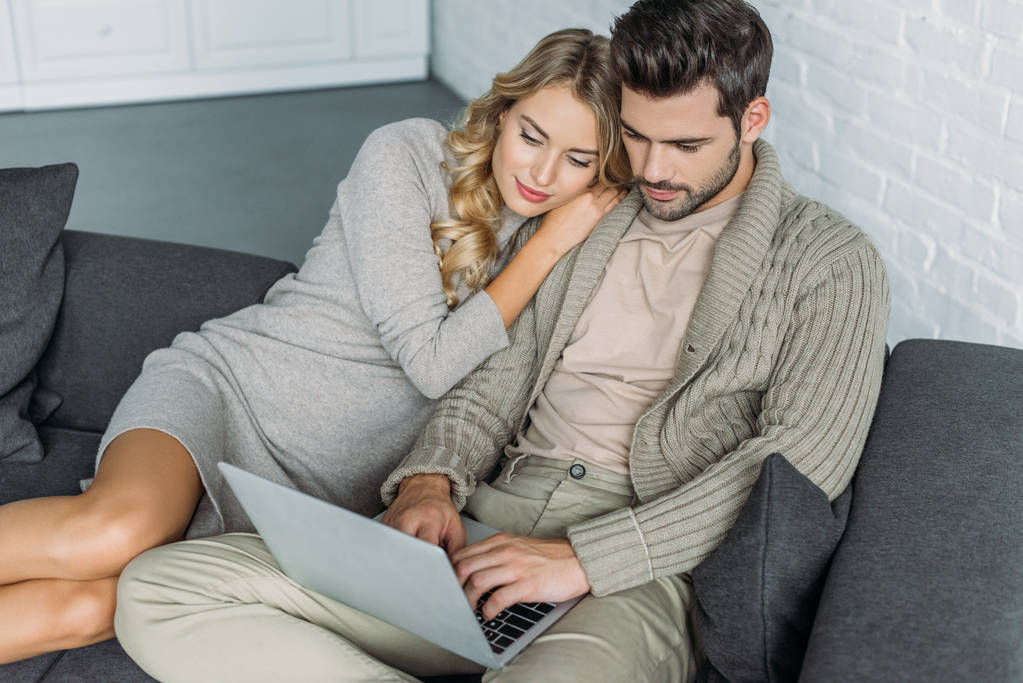 visão de alto ângulo de belo jovem casal sentado no sofá juntos e usando laptop em casa
 - Foto, Imagem