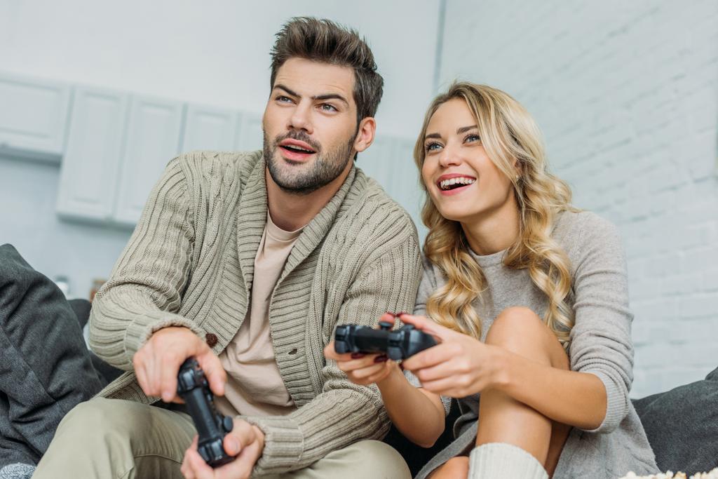 улыбающаяся молодая пара, играющая вместе в видеоигры на диване дома
 - Фото, изображение