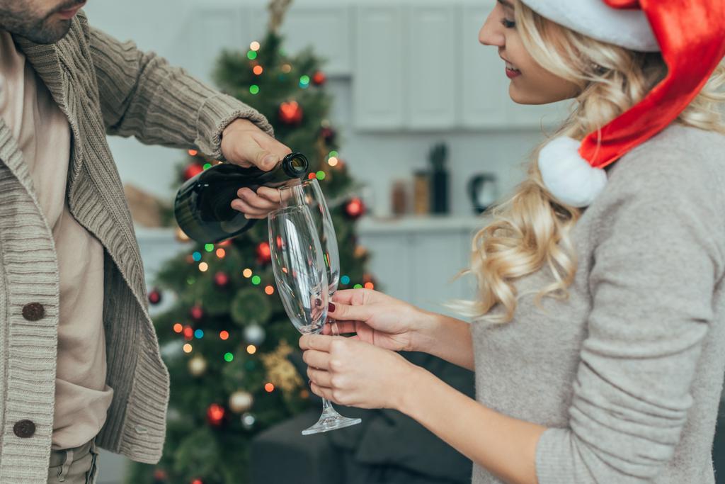 rajattu kuva nuori pari kaatamalla samppanjaa lasit edessä joulukuusi kotona
 - Valokuva, kuva