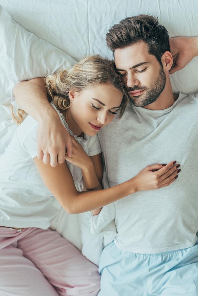 pohled shora šťastný mladý pár spolu vyspí a objímání v posteli doma - Fotografie, Obrázek