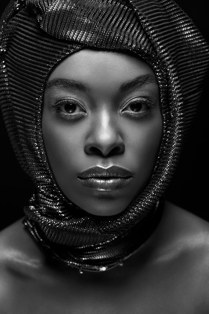 Schwarz-Weiß-Foto einer stilvollen afrikanisch-amerikanischen Frau, die isoliert auf schwarz in die Kamera blickt - Foto, Bild