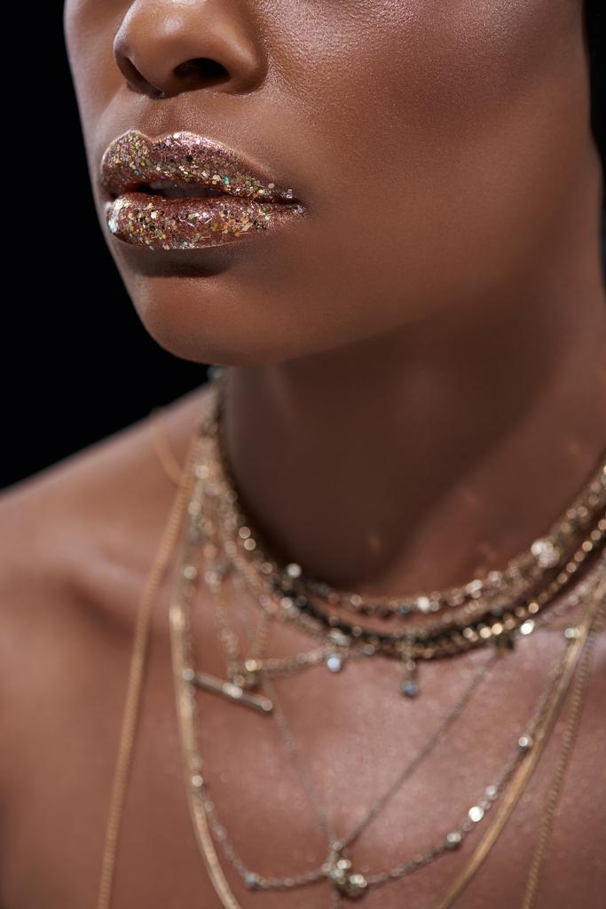 обрезанный снимок африканской американки с блестящим блеском для губ, изолированный на черном
 - Фото, изображение