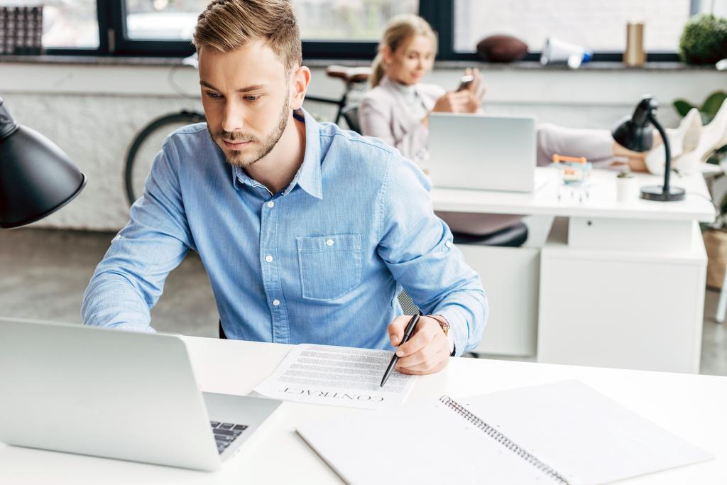 młody biznesmen za pomocą laptopa i pracy z umowy w biurze - Zdjęcie, obraz