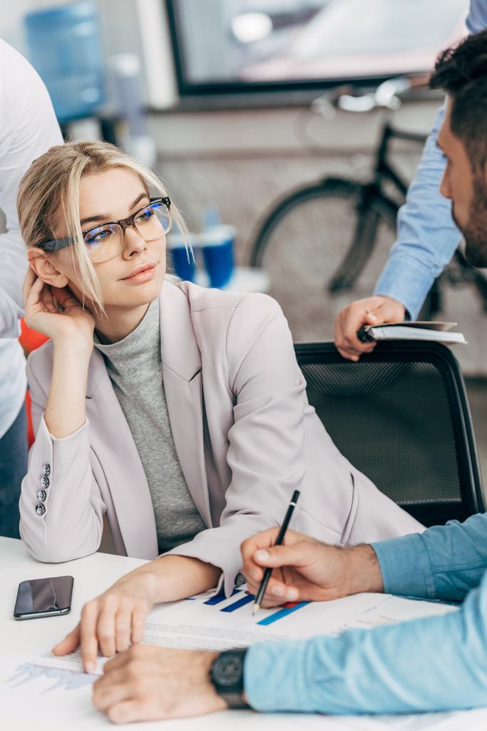 уверенная молодая бизнесвумен в очках смотрит на коллег мужского пола в офисе
 - Фото, изображение