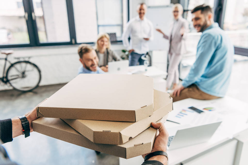 обрезанный снимок человека, приносящего пиццу счастливым коллегам в офисе
 - Фото, изображение