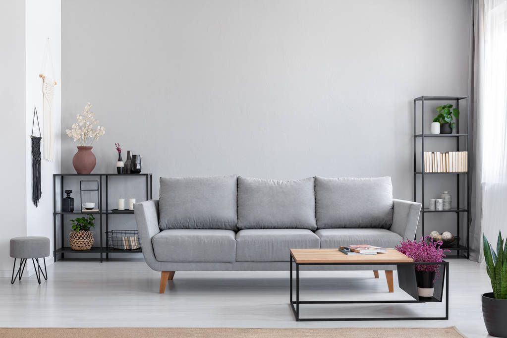Fiori in tavolo di legno di fronte a divano grigio in moderno appartamento semplice interno con sgabello. Foto reale
 - Foto, immagini
