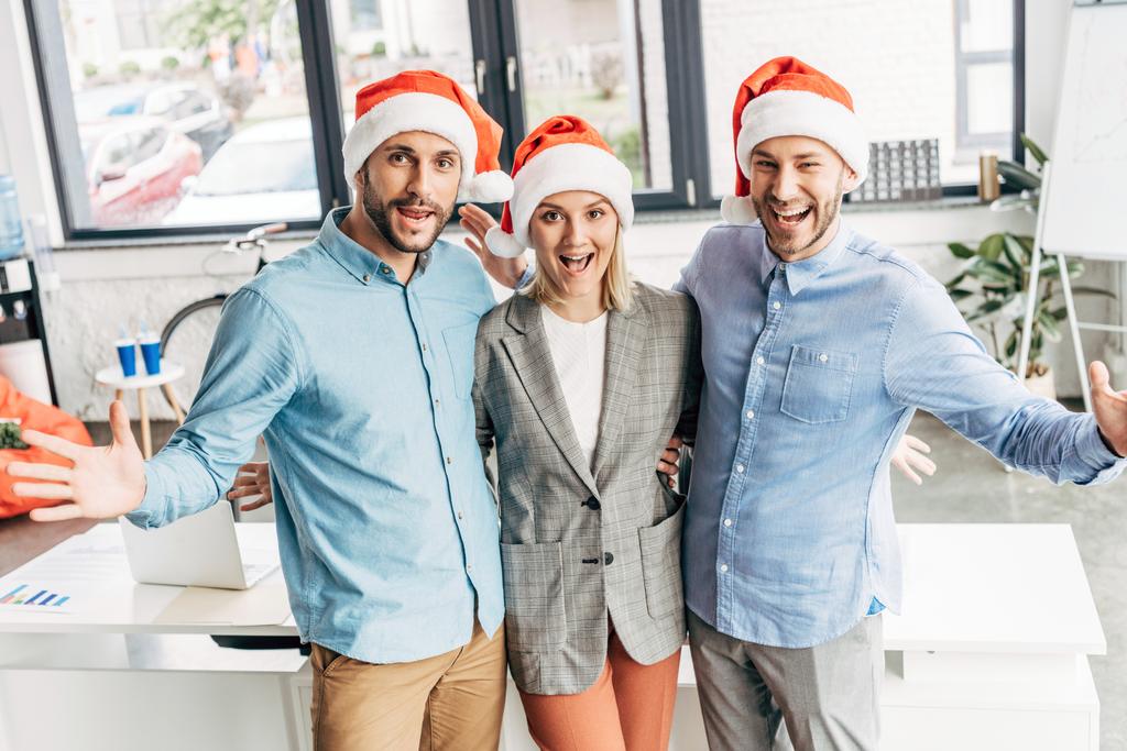 веселая молодая команда бизнесменов в шляпах Санты улыбается в офисе перед камерой
 - Фото, изображение