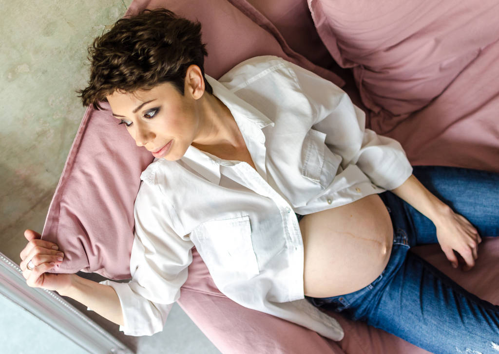 Bela mulher grávida sentada no sofá em casa
 - Foto, Imagem