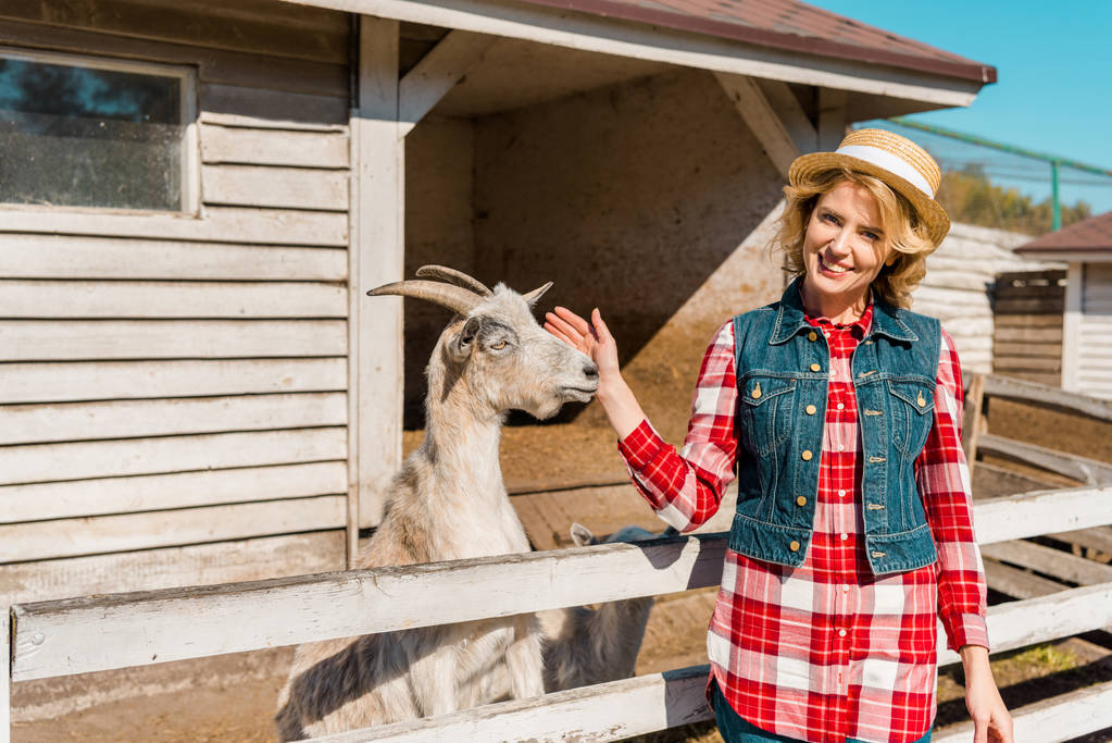 dla dorosłych samica rolnika, dotykając Koza w pobliżu drewniany płot ranczo - Zdjęcie, obraz