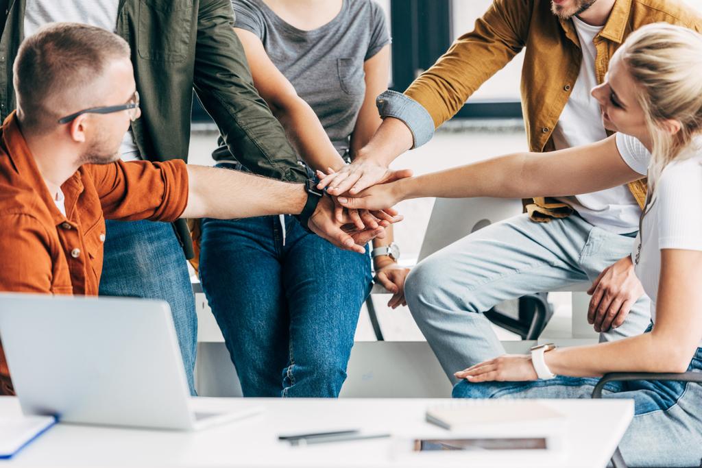foto recortada de grupo de jovens empreendedores fazendo gesto de equipe enquanto trabalham na startup juntos no escritório
 - Foto, Imagem