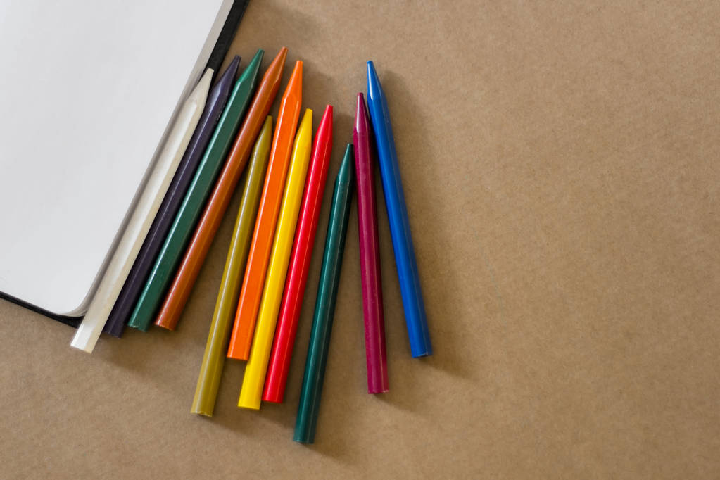 Reeks van kleurrijke ranndomly geregeld pensils met open lege laptop voor het schetsen op de lichte bruine achtergrond van Kraft papier met kopie ruimte. - Foto, afbeelding