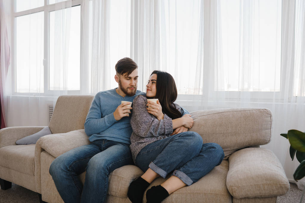 junges Paar sitzt auf Sofa mit heißen Getränken - Foto, Bild