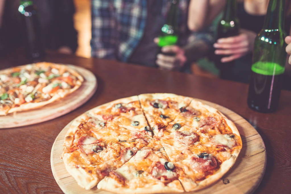 Amigos sentados en una mesa de madera en un bar con cervezas y pizza
. - Foto, Imagen