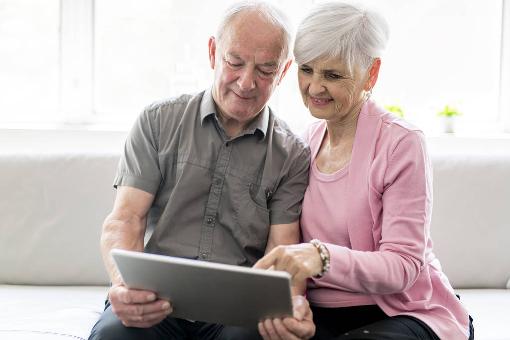 Affettuosa coppia di anziani attraenti seduti insieme su un divano con tablet
 - Foto, immagini