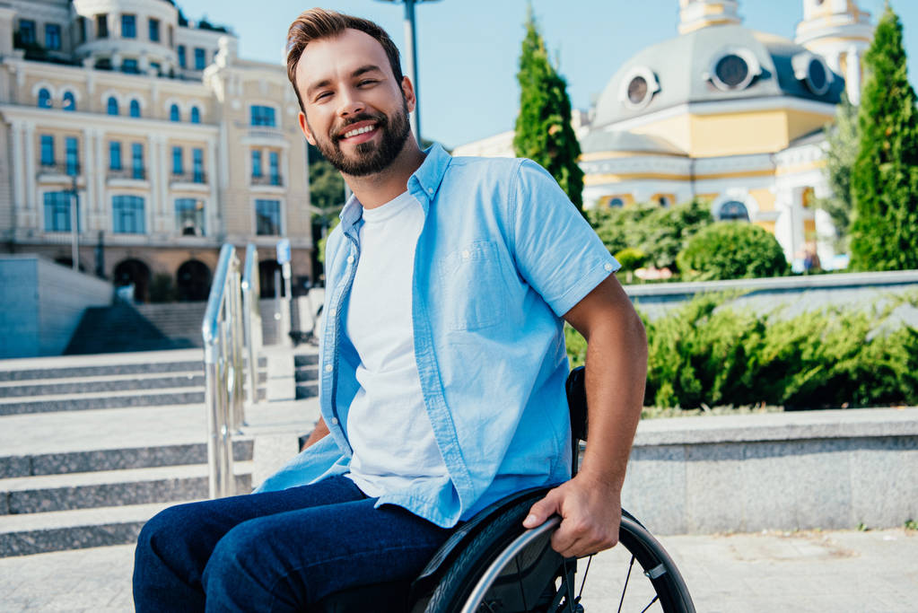 cheerful handsome man in wheelchair looking at camera on street - Photo, Image