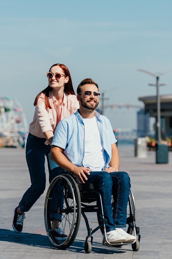 ελκυστική κοπέλα πιέζει όμορφος απενεργοποιημένη φίλος σε αναπηρικό αμαξίδιο επί της οδού - Φωτογραφία, εικόνα