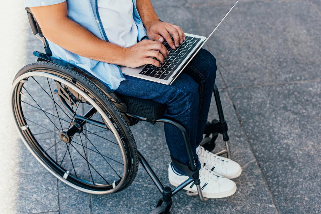image recadrée de l'homme en fauteuil roulant en utilisant un ordinateur portable dans la rue
 - Photo, image