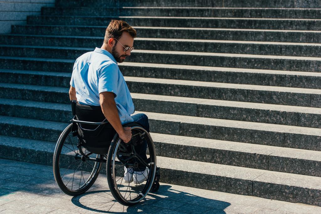 komea vammainen mies, joka käyttää pyörätuolia kadulla ja pysähtyy lähellä portaita ilman luiskaa
 - Valokuva, kuva
