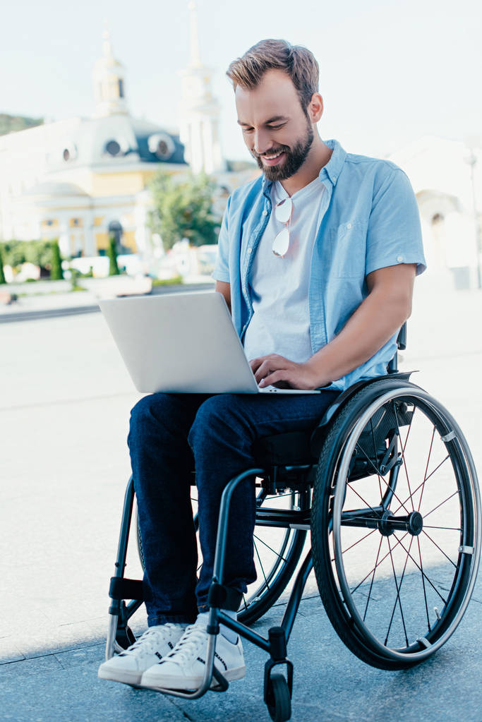 όμορφος άνδρας σε αναπηρικό αμαξίδιο που χρησιμοποιούν φορητό υπολογιστή στην οδό - Φωτογραφία, εικόνα