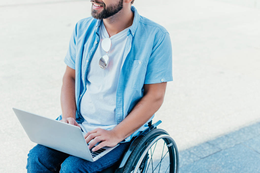 Schnappschuss eines bärtigen Mannes im Rollstuhl mit Laptop auf der Straße - Foto, Bild