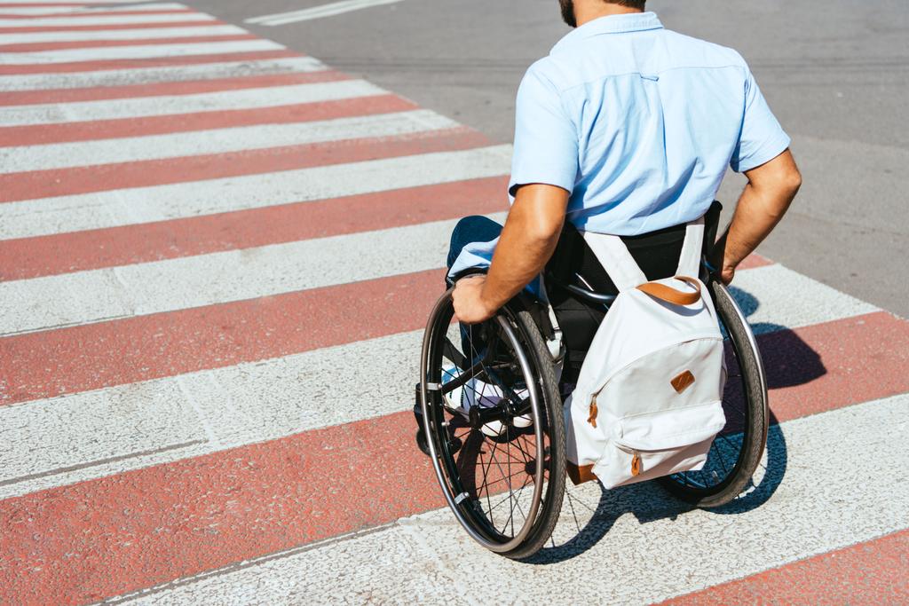 περικομμένη εικόνα του ανθρώπου που χρησιμοποιούν αναπηρικό αμαξίδιο στη διάβαση πεζών επί της οδού - Φωτογραφία, εικόνα