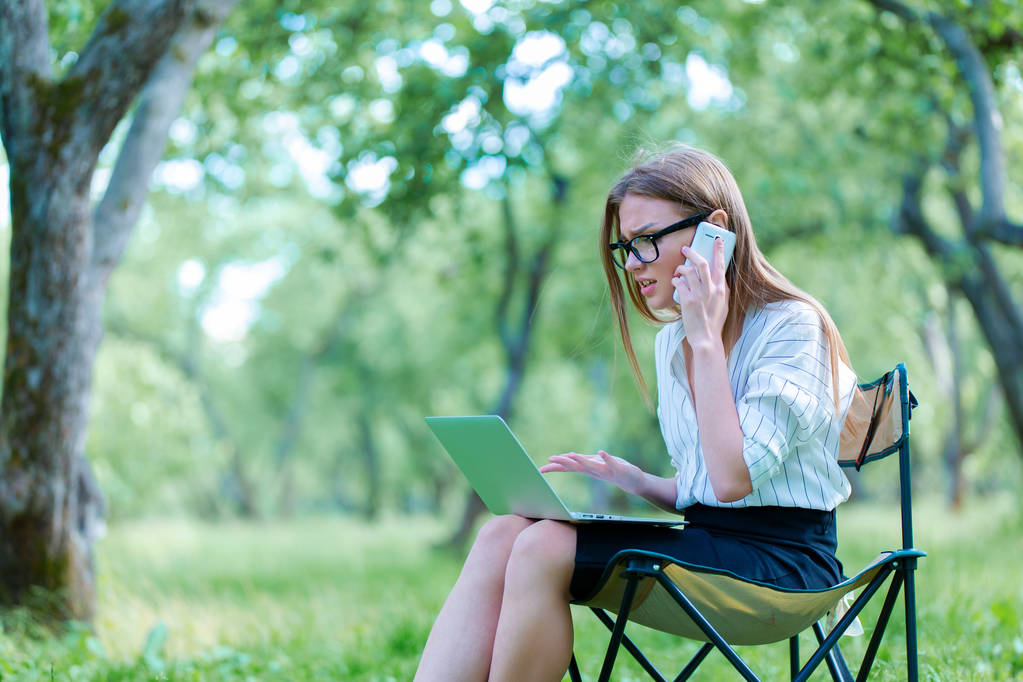Dziewczyna rozmawia przez telefon i pracy przy komputerze w parku - Zdjęcie, obraz