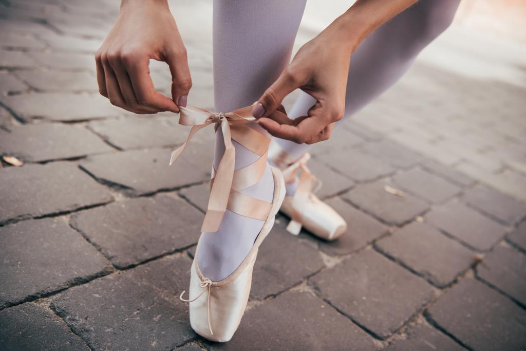 tiro cortado de jovem bailarina amarrando sapato pointe na rua
 - Foto, Imagem