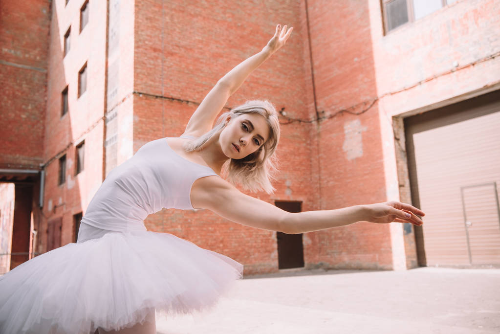 lage hoekmening van jonge ballerina camera kijken tijdens het dansen op straat - Foto, afbeelding