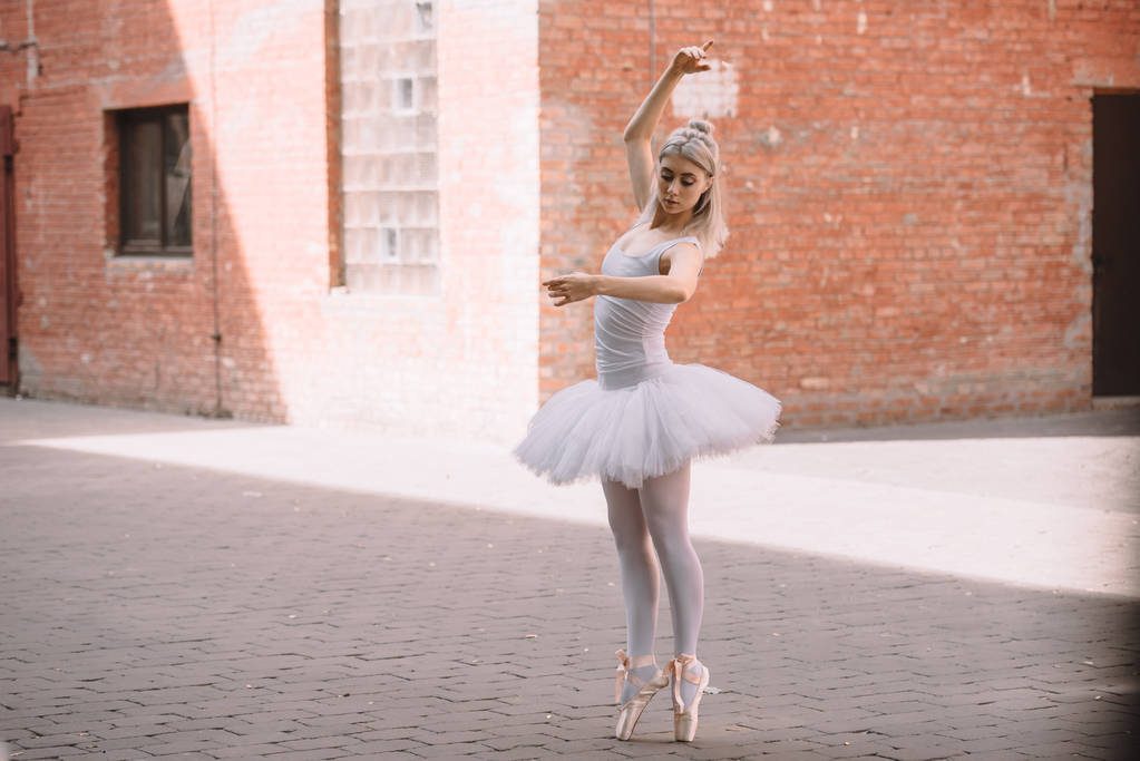 young ballerina in white tutu and pointe shoes dancing on street   - Photo, Image
