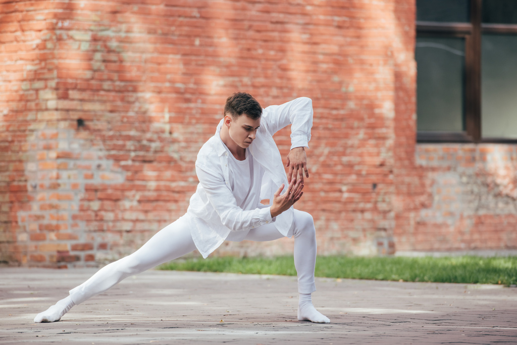 όμορφος νεαρό άντρα χορευτή σε λευκά ρούχα εξάσκηση στην οδό   - Φωτογραφία, εικόνα